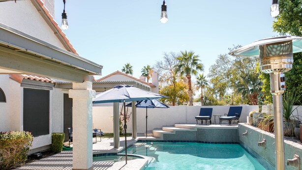 Ein Pool mit gefliestem Deck, Liegestühlen und einer Pergola mit Sonnenschirmen.