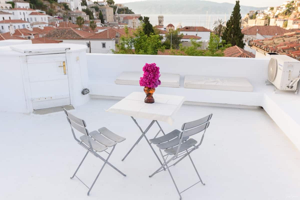 Una terraza en la azotea con una mesa, dos sillas, un sofá y un jarrón de flores.