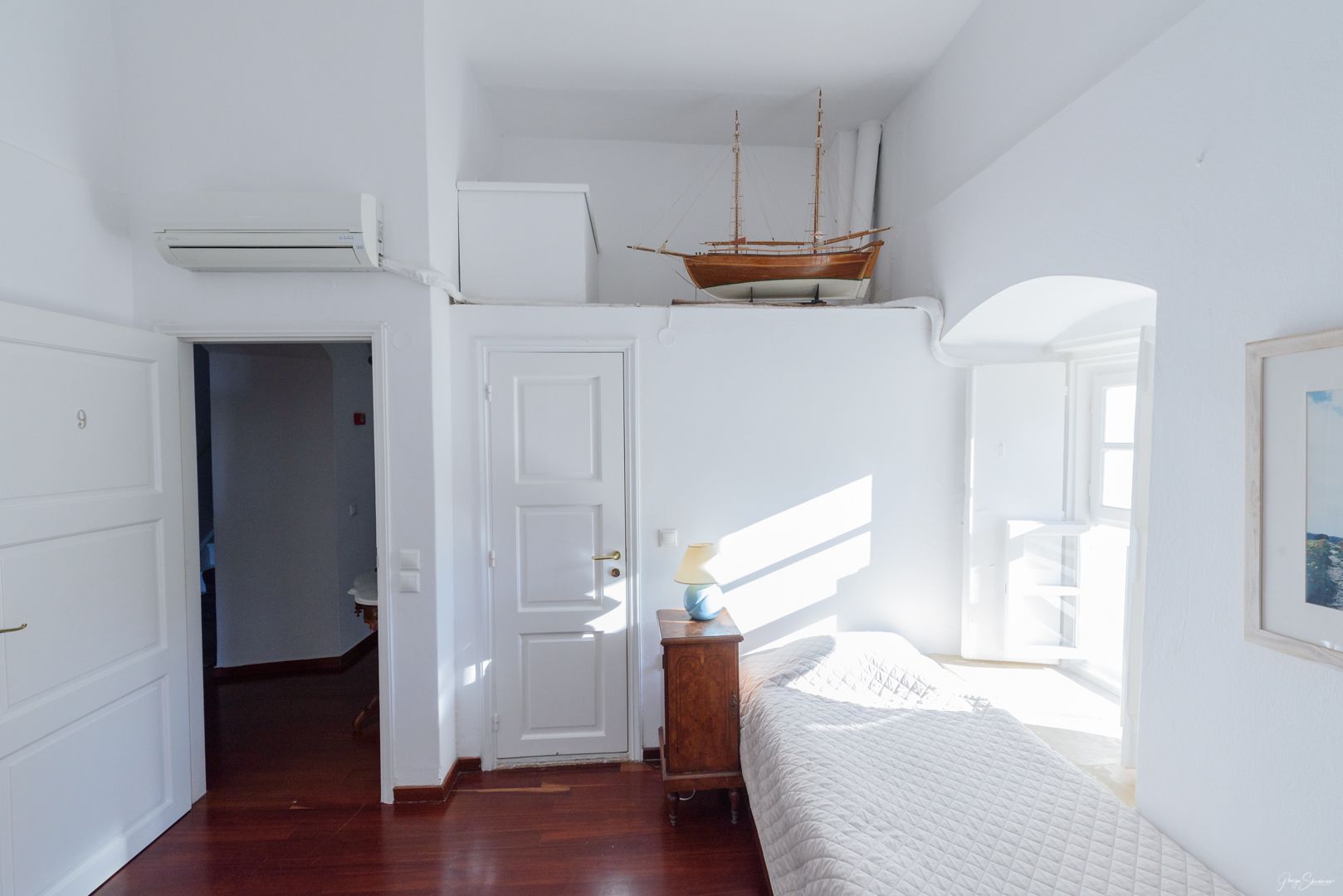 Un dormitorio con techo inclinado, una cama, una mesita de noche de madera, una lámpara y un modelo de barco.