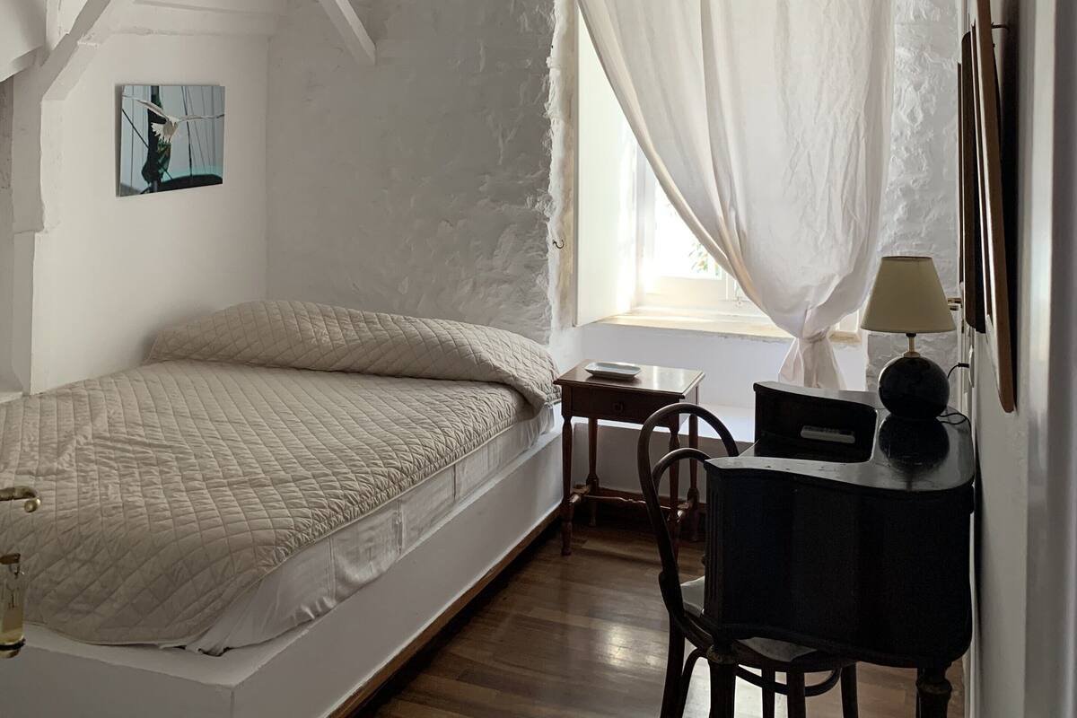 Un dormitorio con cama, escritorio, silla, lámpara y ventana con cortinas.
