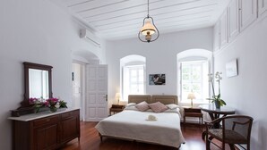 Un dormitorio con una cama grande, un aparador, una silla y un escritorio. Hay una ventana y una puerta en la habitación.