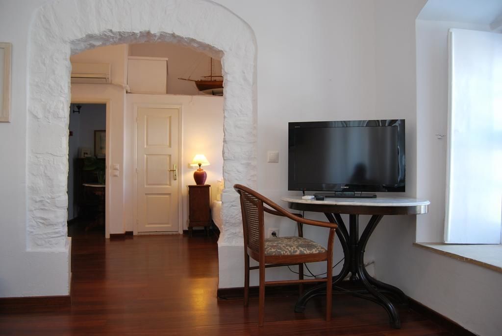 A room with a television on a table, a chair, and a door leading to another room.