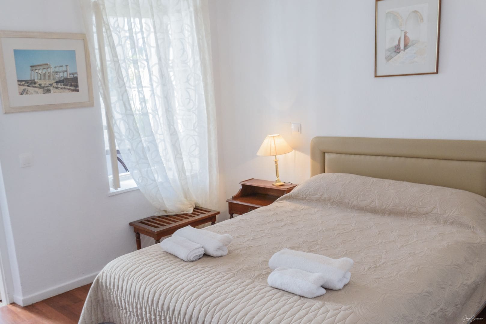 A neatly made bed with two rolled towels, a bedside lamp, and a framed picture on the wall.