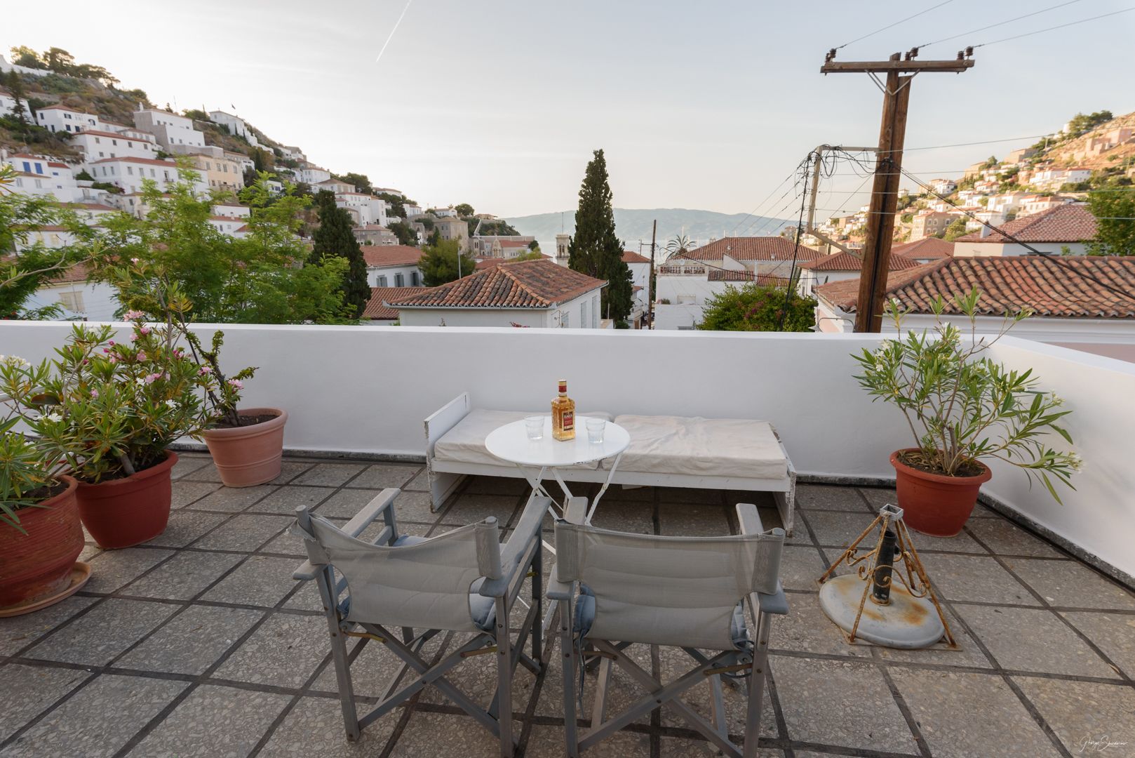 A terrace with a table and chairs, potted plants, and a view of a hillside town.