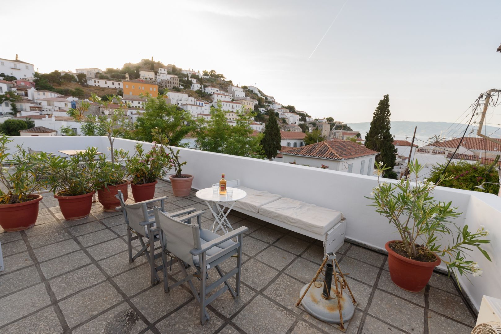 A rooftop terrace with a white table, chairs, and potted plants.