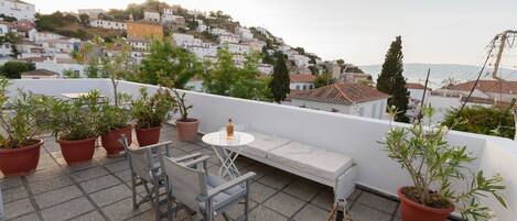 A rooftop terrace with a white table, chairs, and potted plants.