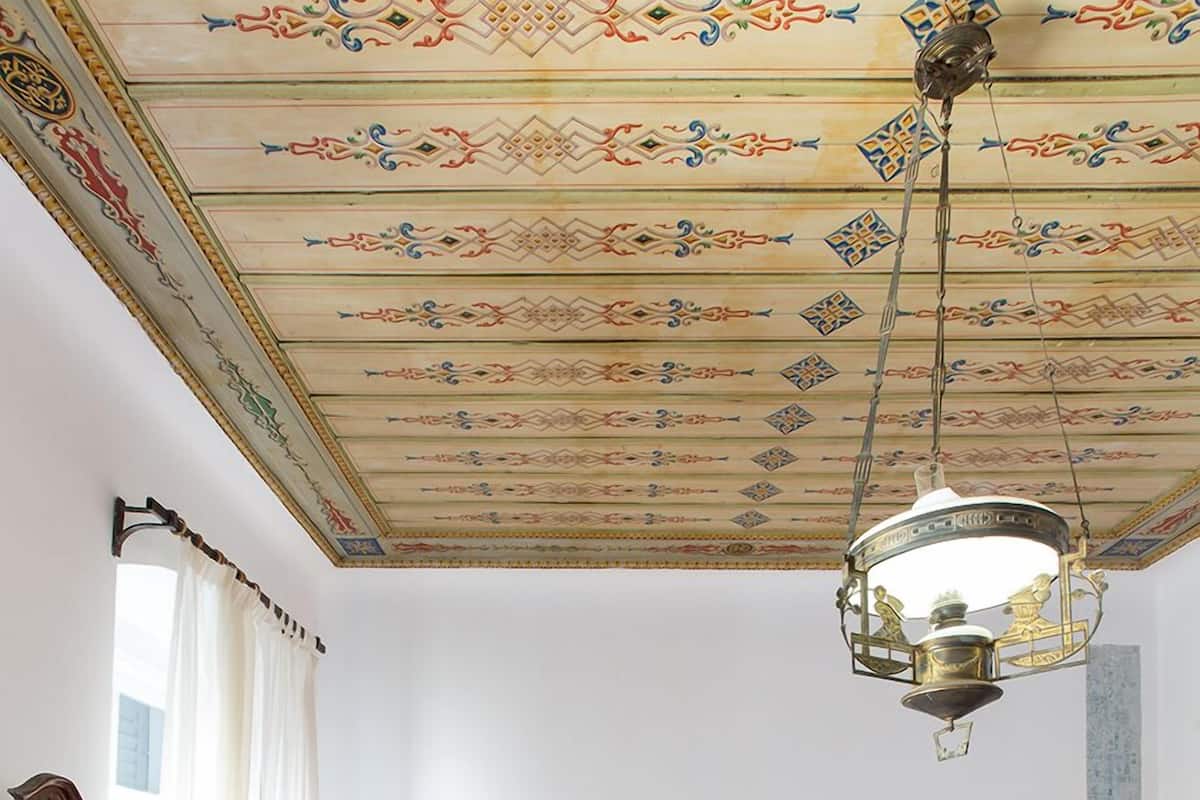 Un dormitorio con una cama grande, un aparador de madera, dos mesitas de noche con lámparas y un techo con diseños intrincados.