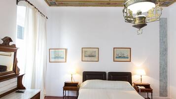 Habitación de hotel con una cama grande, dos mesitas de noche con lámparas, un aparador de madera y un techo decorativo.