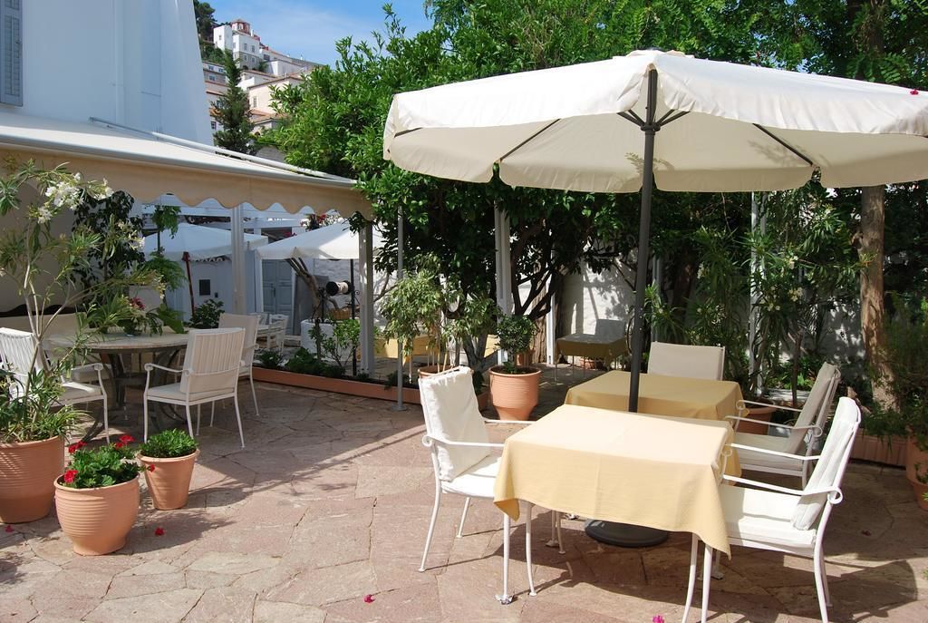 Une terrasse extérieure avec des chaises et des tables blanches, protégée par un grand parasol et entourée de plantes en pot.