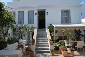 A building with a staircase leading to a door, surrounded by potted plants and outdoor seating.