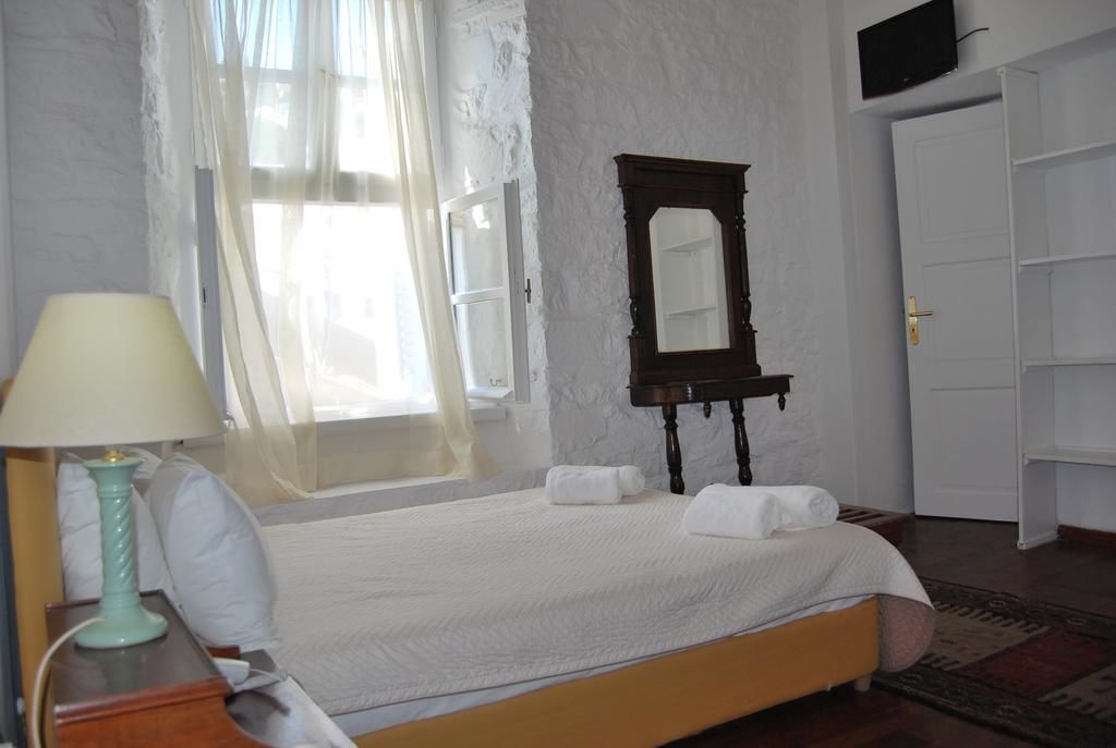 A neatly made bed with white linens, a wooden nightstand with a lamp, a large mirror, and a wardrobe.
