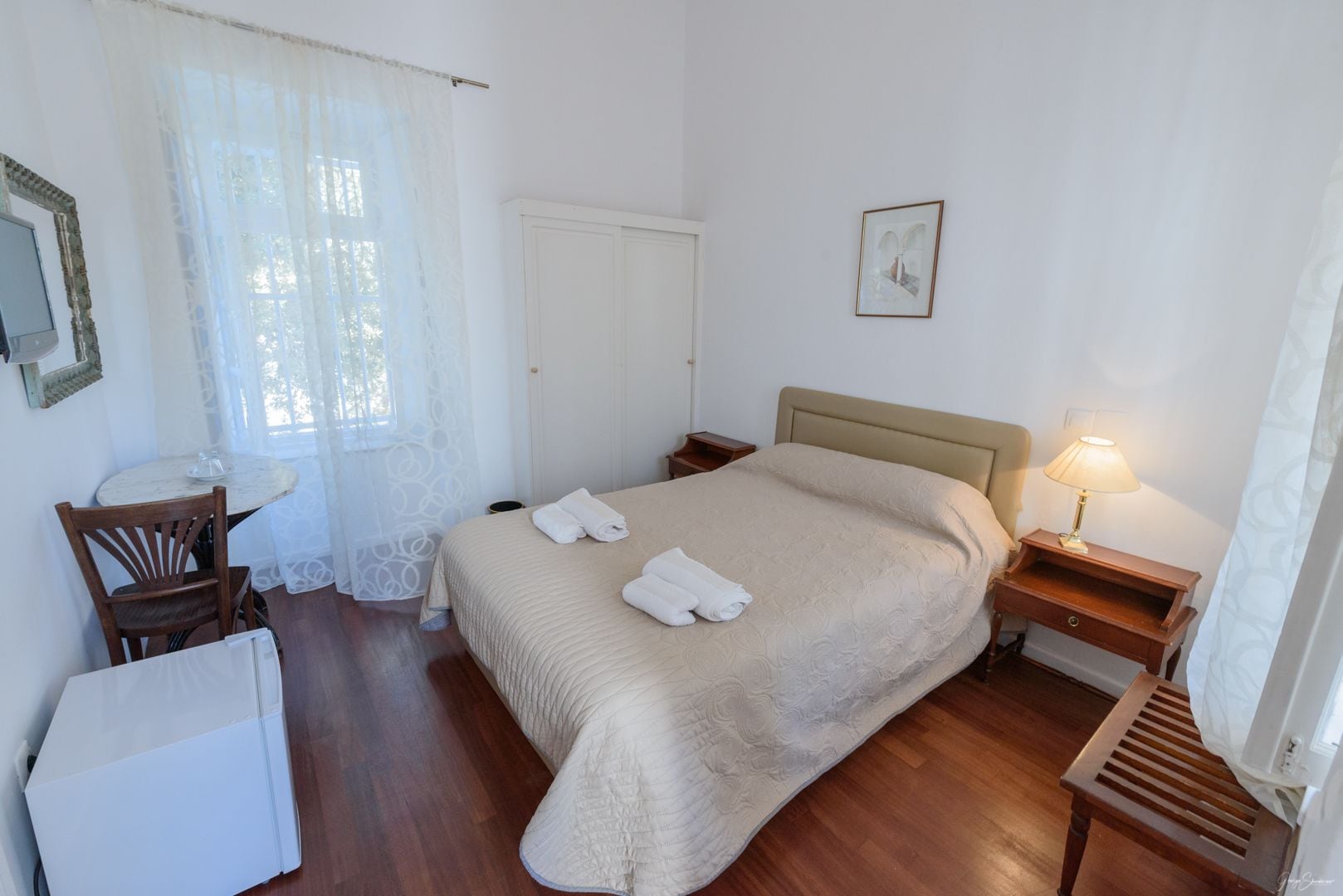 Une chambre bien rangée, avec un lit, une table de chevet, une lampe, une chaise et une petite table sur laquelle se trouve une autre lampe.