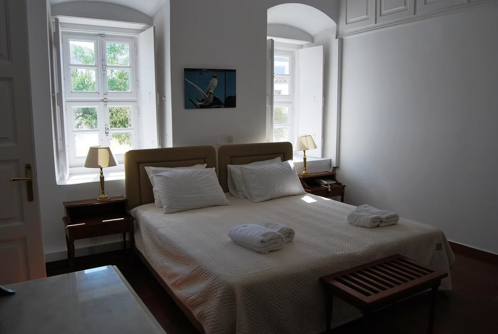 A hotel room with a large bed, two bedside tables with lamps, a bench at the foot of the bed, and a painting on the wall.