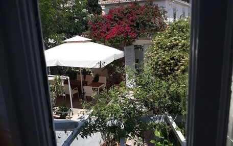 A view of a courtyard with a white umbrella, a table, and chairs. There is a building with a tiled roof in the background.