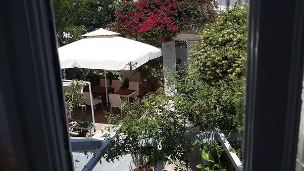 Vista de un patio con un paraguas blanco, una mesa y sillas. Se observa un edificio con tejado de baldosas al fondo.
