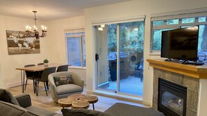A modern living room with a fireplace, a dining area, and a large sliding glass door leading to a patio. - Amazing location steps from Whistler Village, with outdoor heated pool/hot tub! (Whistler)