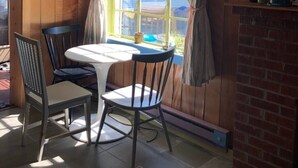 Een kamer met houten wanden, een tafel met stoelen, een raam met gordijnen, een schilderij aan de muur en een bakstenen open haard.