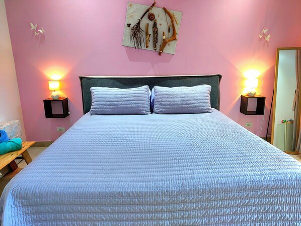 A bedroom with a bed, two bedside lamps, a nightstand, a wall-mounted artwork, and a door. - Casita Mar Y Posa (Tempate)