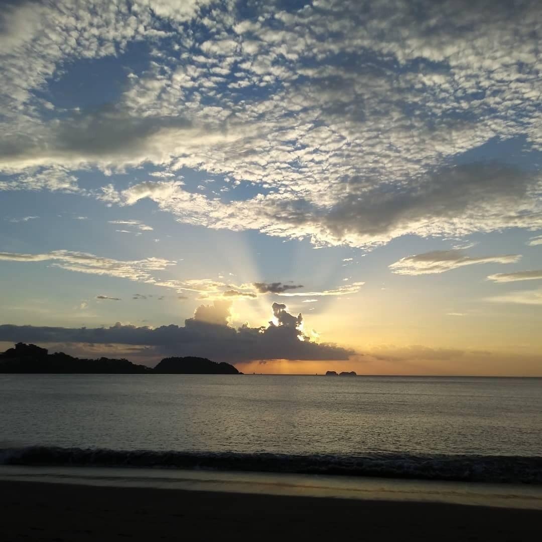 A beach scene with a sunset, calm sea, and distant landforms.