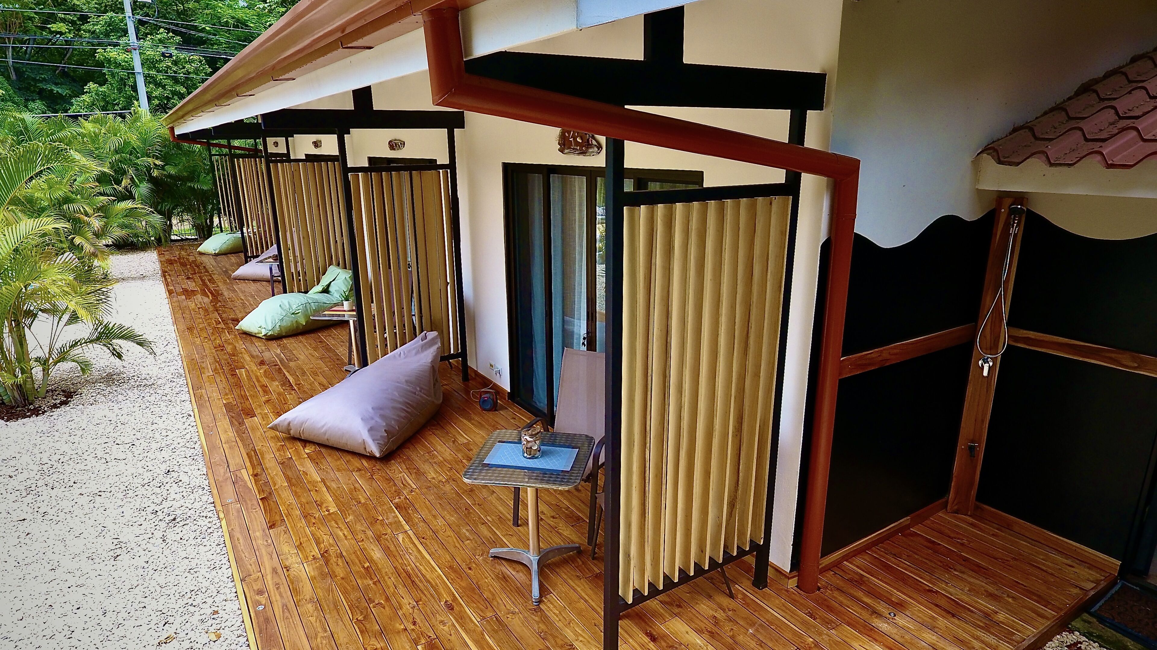 A covered outdoor seating area with wooden flooring, cushioned seating, and a small table.
