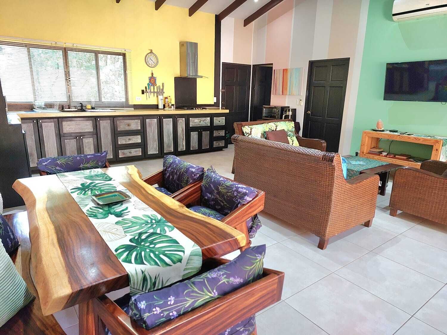 Uma sala de estar com área de jantar, sofá, televisão e cozinha com armários e janela.