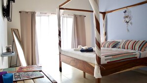 Un lit à baldaquin avec une couvre-lit à rayures, une table de chevet avec un miroir et des livres, et un attrape-rêves accroché au mur.