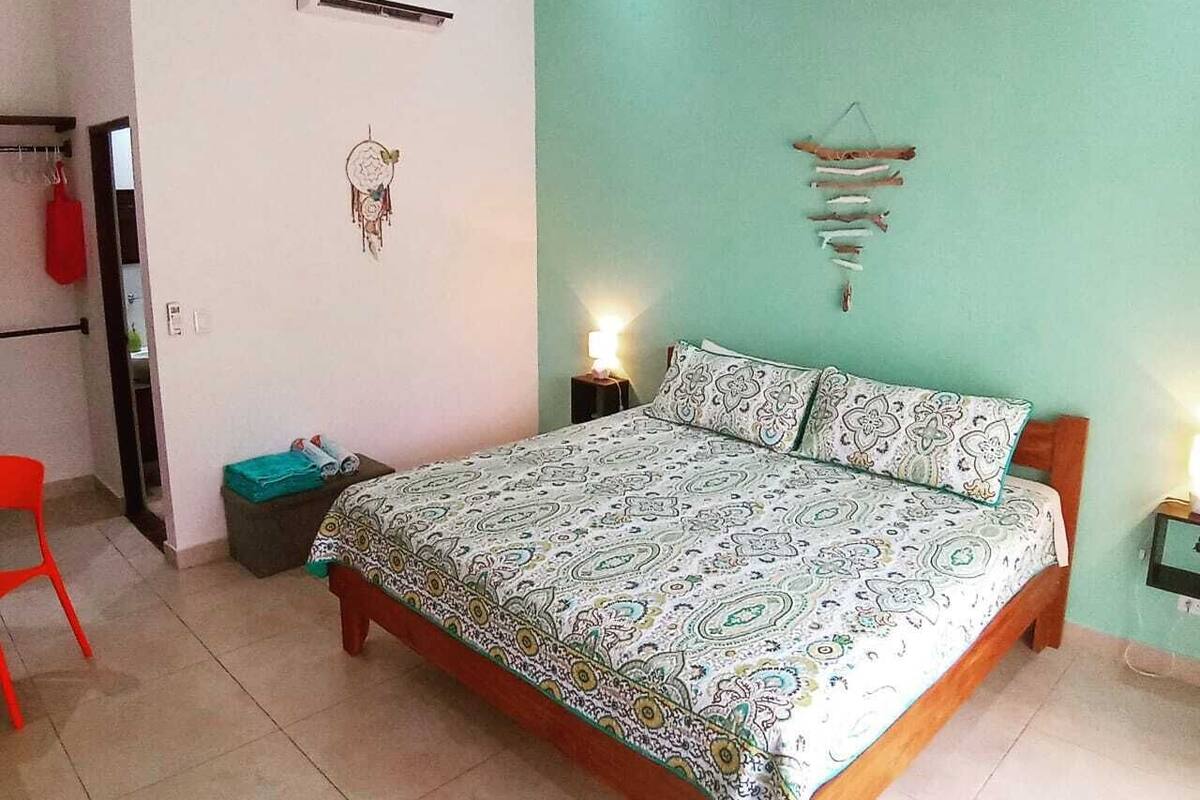 Une chambre à coucher comprenant un lit, un ventilateur de plafond, un climatiseur, un attrape-rêves et un élément de décoration murale.