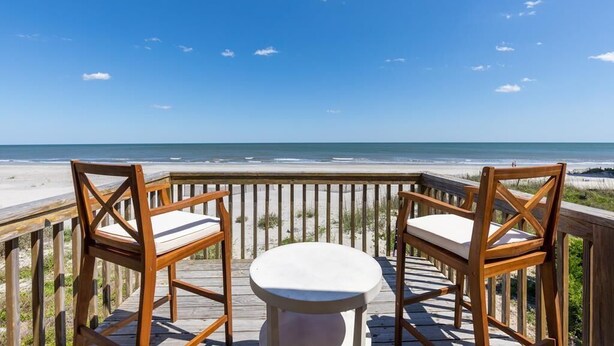 A wooden deck with two chairs and a small table, overlooking a beach. - Discounted rates! The Edge of the Edge of America! (Folly Beach)