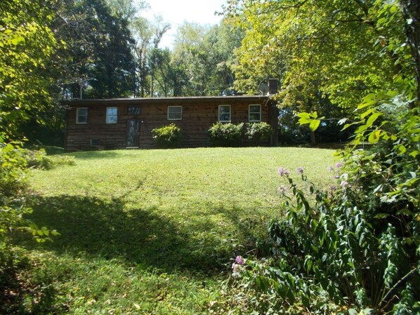Un chalet rustique en rondins de bois, doté d’une pelouse bien entretenue et entouré de verdure.