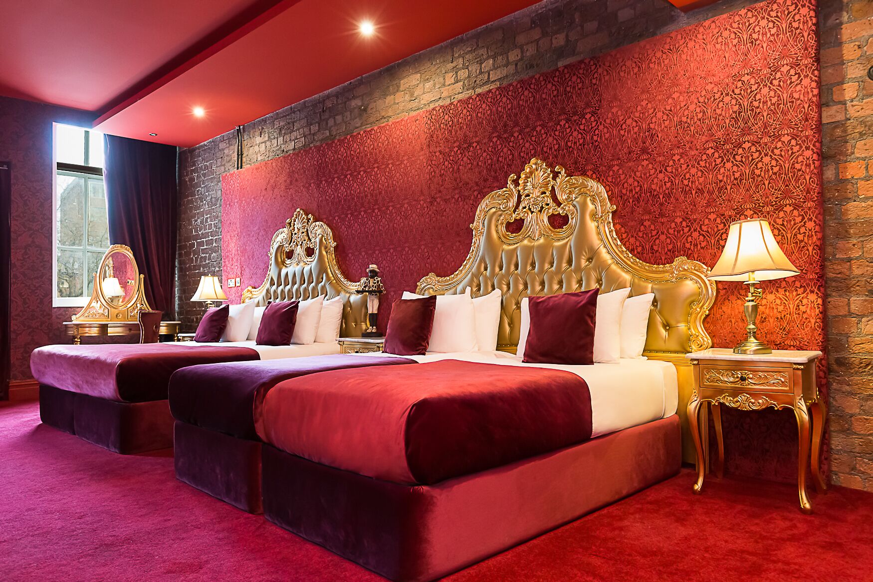 Une chambre d’hôtel luxueuse, dotée de deux grands lits, de têtes de lit richement décorées et d’une moquette rouge.