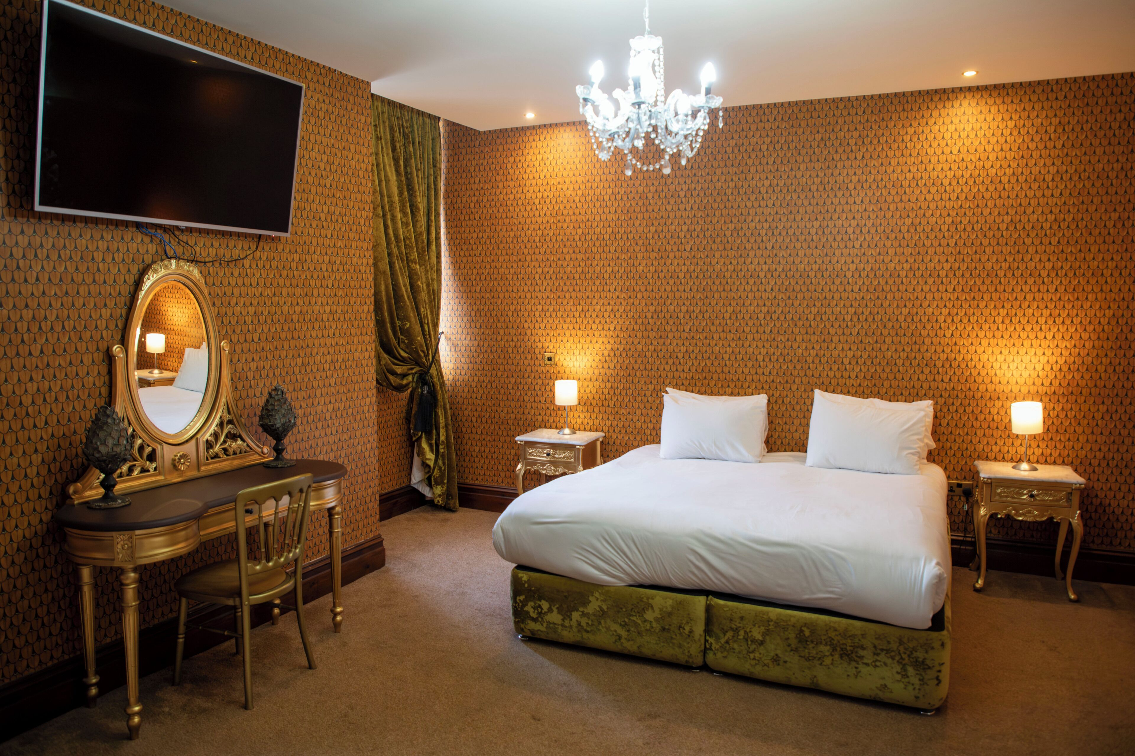 Een hotelkamer met een groot bed, een bureau met spiegel, twee nachtkastjes met lampen en een kroonluchter.