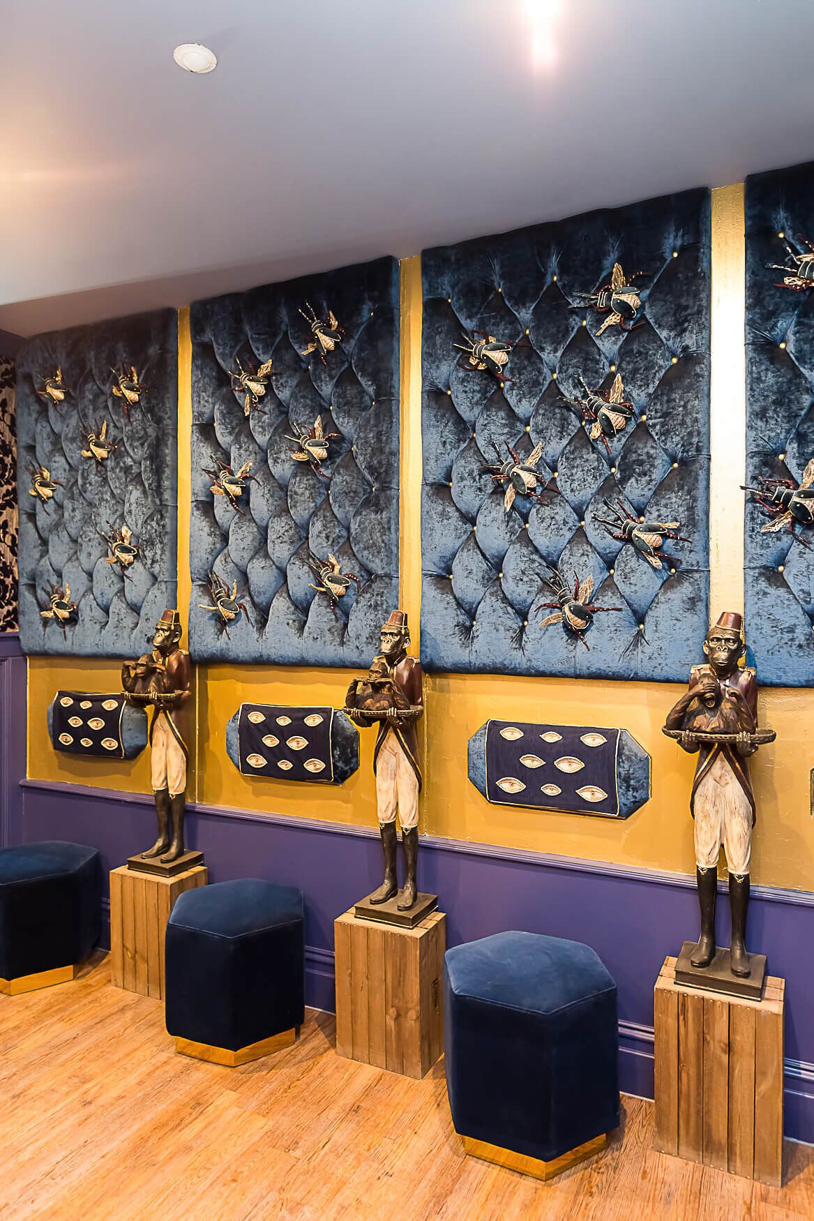 A room with a patterned wall, wooden stools, and a statue of a man holding a drum.