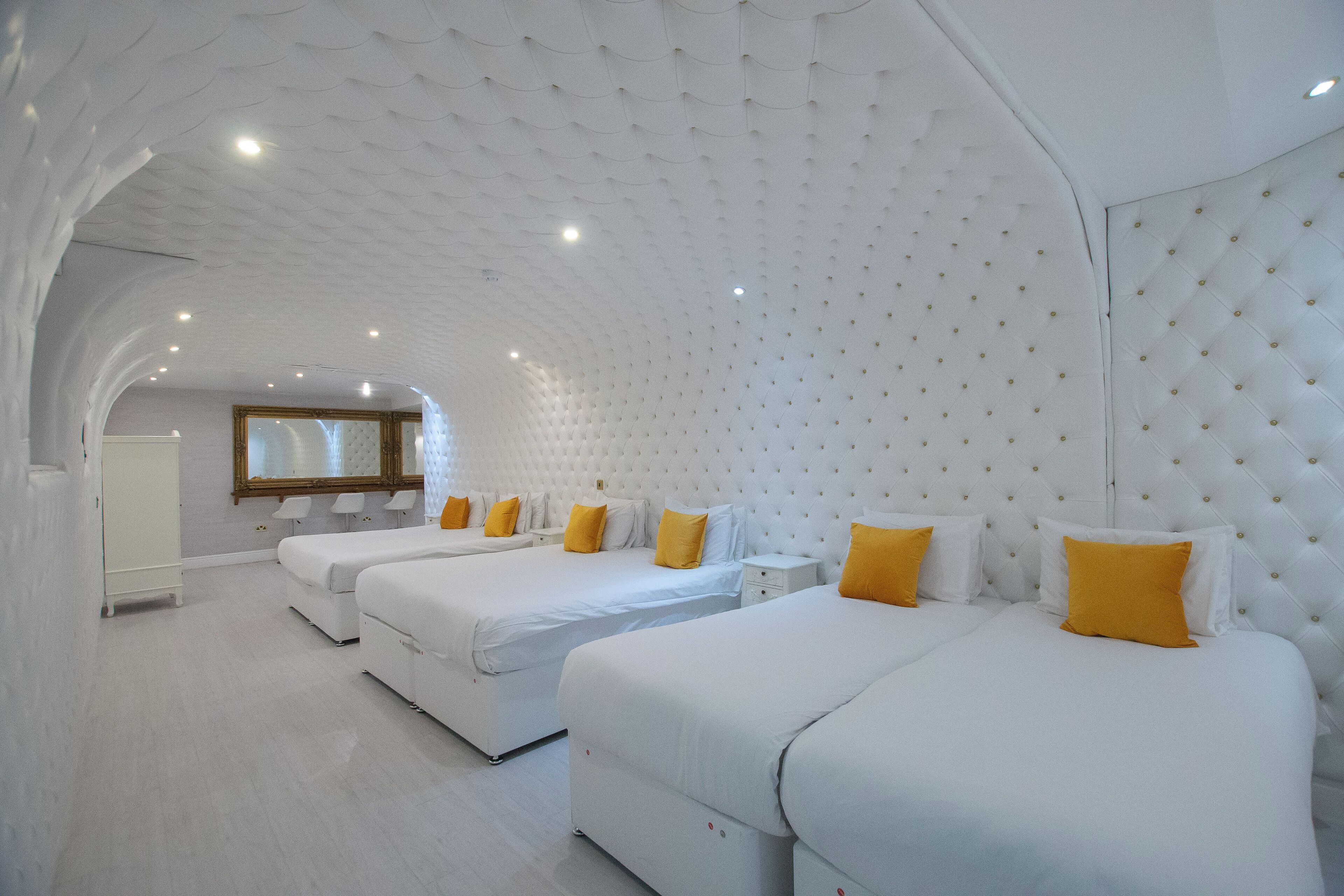 A hotel room with three beds, white bedding, and yellow pillows.