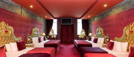 Una lujosa habitación de hotel con dos camas grandes, cabeceros dorados ornamentales, ropa de cama roja y alfombra roja.