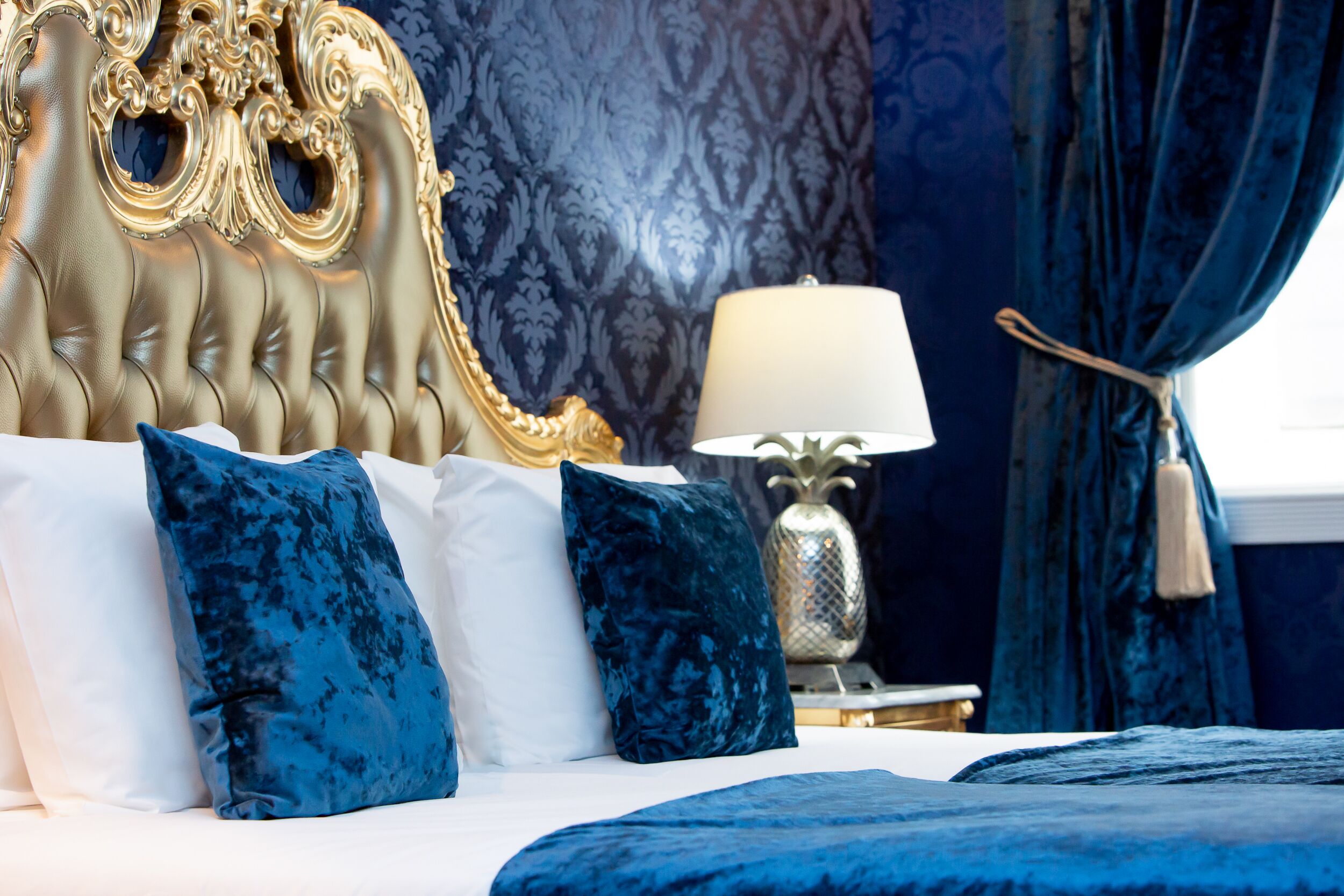 A bed with a tufted headboard, a white and blue color scheme, and a decorative lamp on a bedside table.