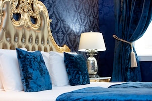 Una cama con cabecera capitonada, decoración en blanco y azul, y una lámpara decorativa sobre una mesita de noche.