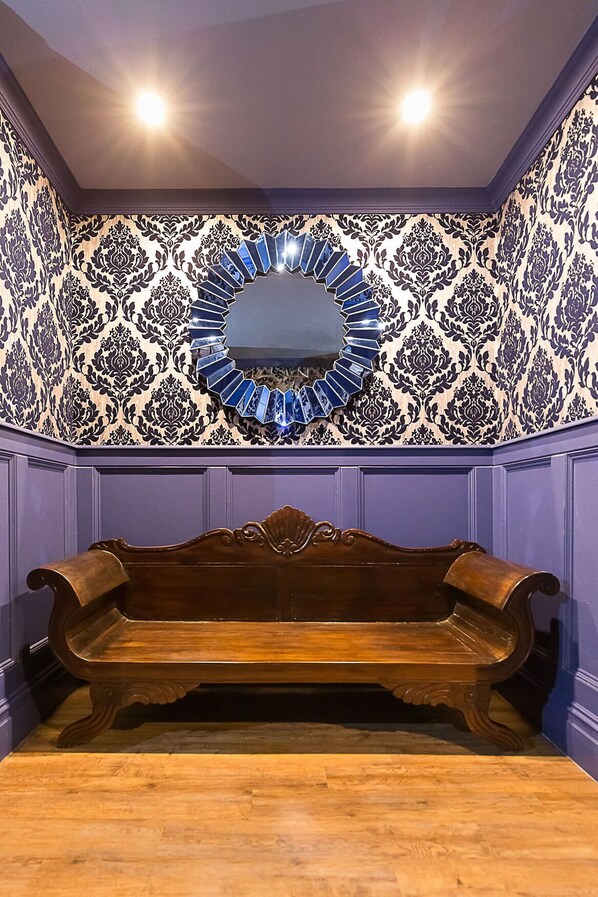 Una habitación con un banco de madera, un espejo decorativo y papel tapiz estampado.