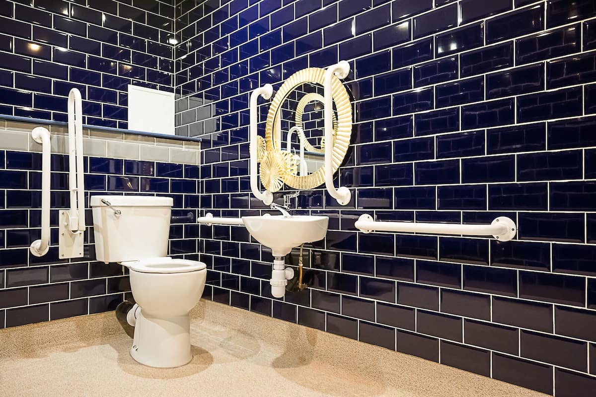 A modern bathroom with a black tiled backsplash, a white toilet, a sink, and a mirror with a decorative frame.