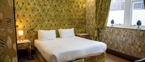 A bedroom with a tufted headboard, a bed with white linens, a nightstand, a lamp, and a window with curtains.