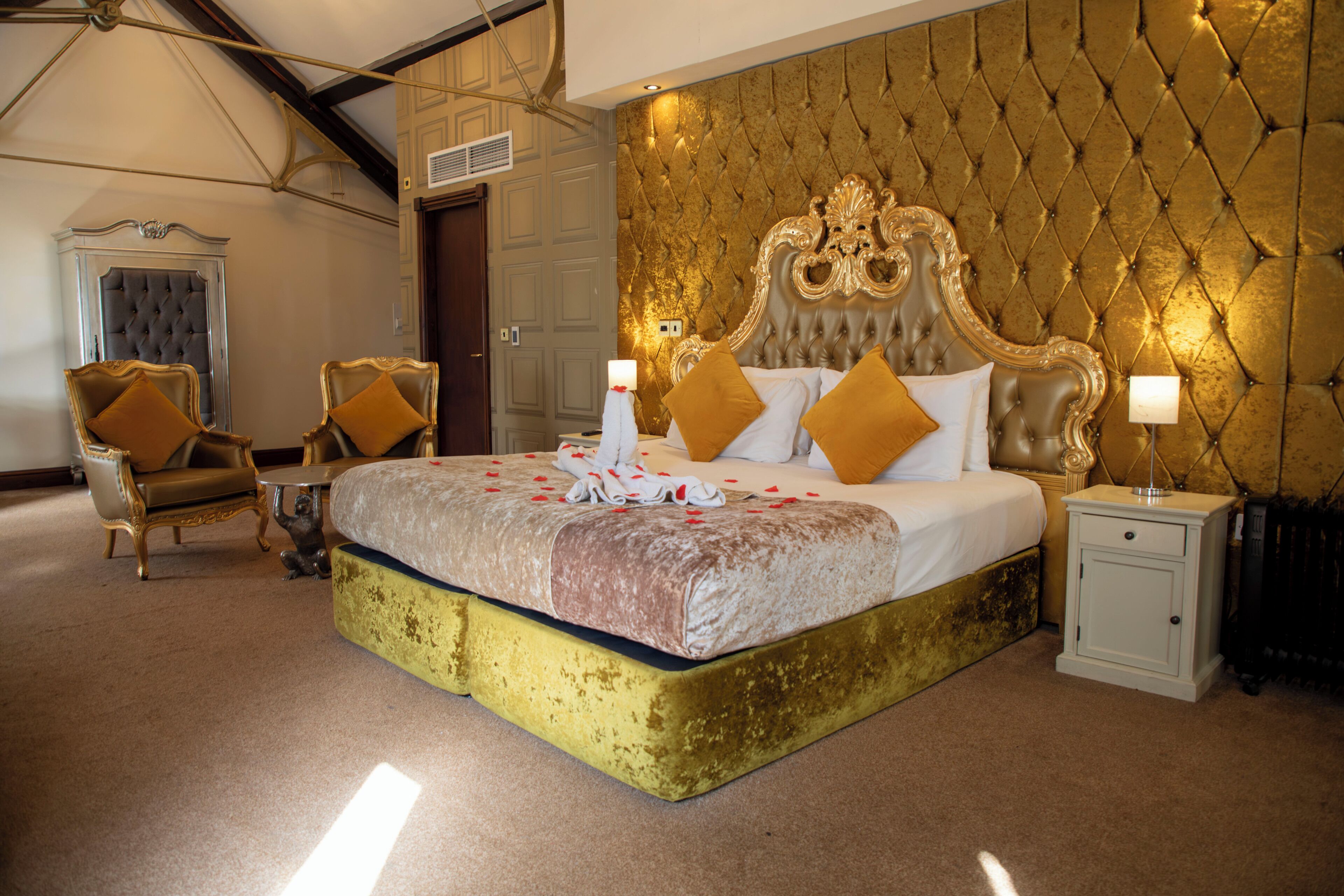 A large bed with a tufted headboard, two armchairs, a nightstand, and a small cabinet.