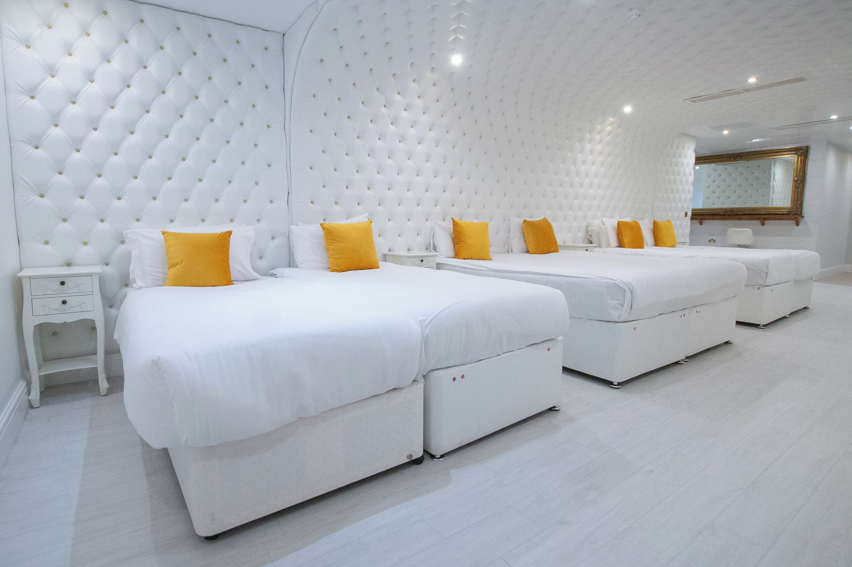 A hotel room with three beds, white bedding, and yellow pillows.