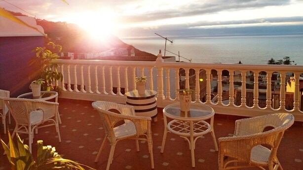 A balcony with wicker furniture, potted plants, and a view of the sea during sunset. - Hotel Drago San Antonio (Icod de los Vinos)