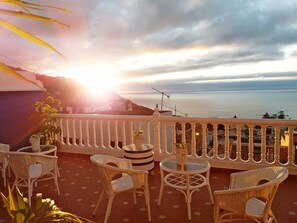 A balcony with wicker furniture, potted plants, and a view of the sea during sunset. - Hotel Drago San Antonio (Icod de los Vinos)