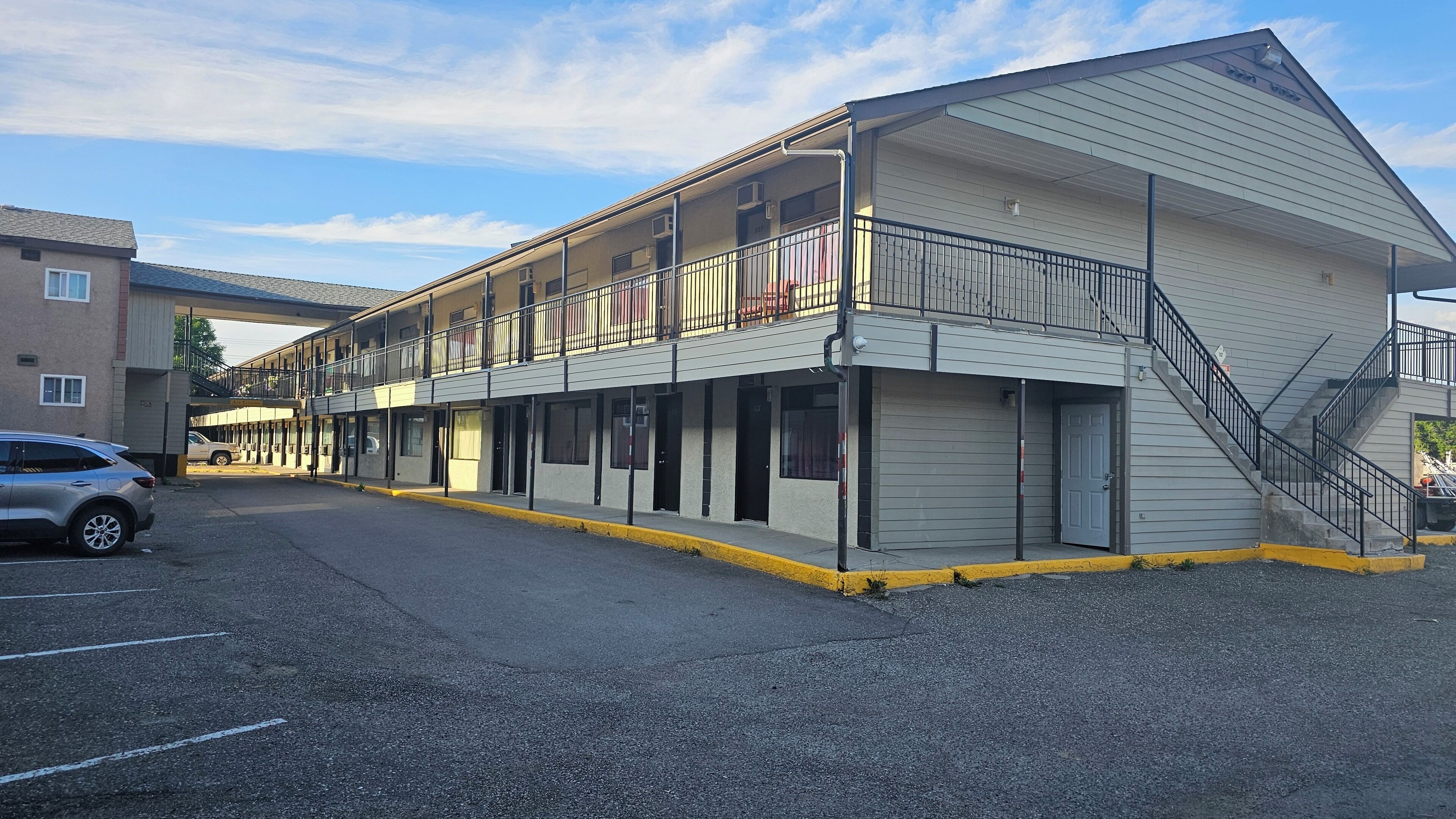 Um motel de vários andares com telhado plano, varandas e estacionamento.