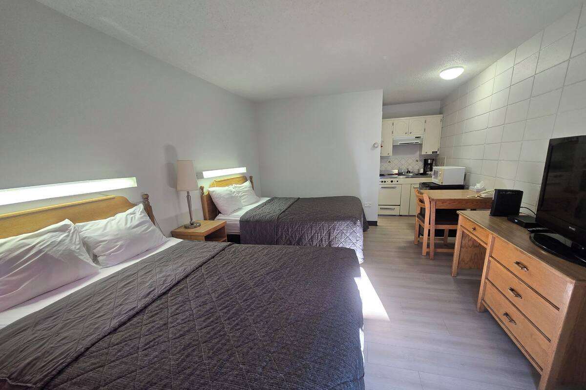 A hotel room with two beds, a desk, a television, and a kitchenette.