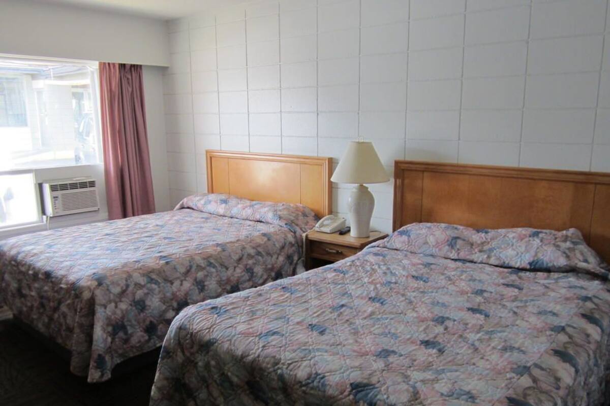A hotel room with two beds, a nightstand with a lamp, a telephone, and a window with curtains.