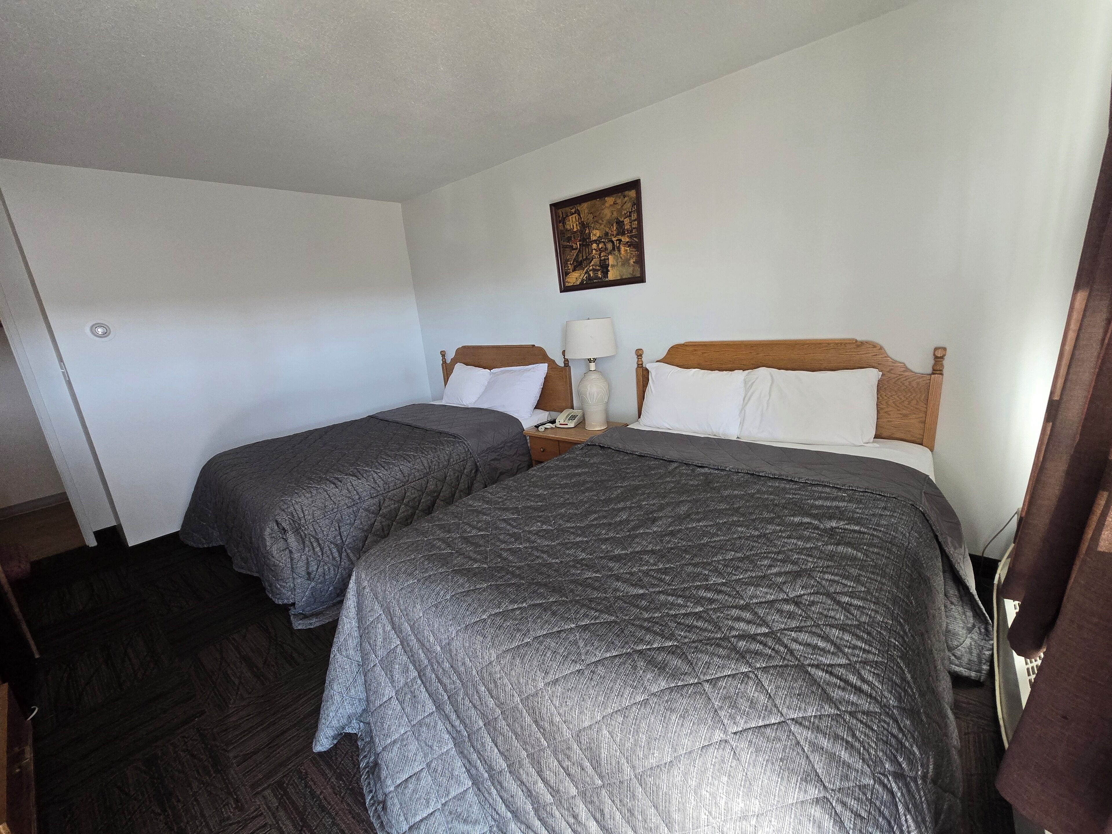 Habitación de hotel con dos camas, una mesita de noche con lámpara, un cuadro en la pared y una puerta.