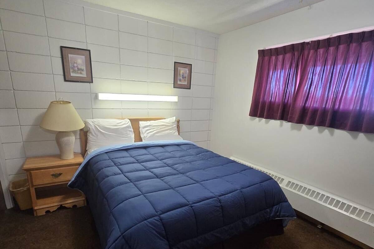 A bedroom with a bed, a nightstand, a lamp, a window with curtains, and a radiator.