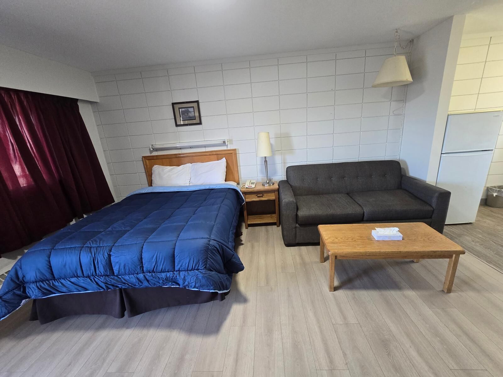 A hotel room with a bed, a sofa, a coffee table, a nightstand, a lamp, and a picture on the wall.
