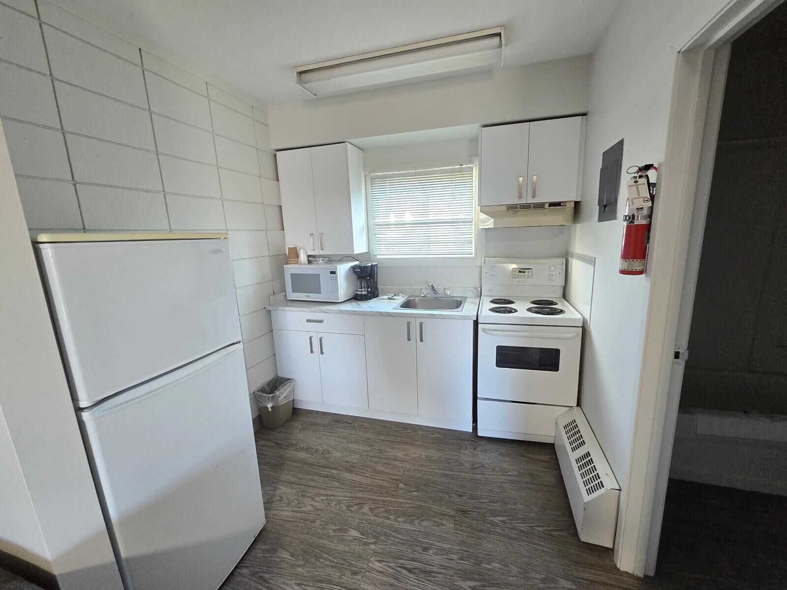 Una cocina compacta con electrodomésticos blancos, microondas, cafetera y estufa.